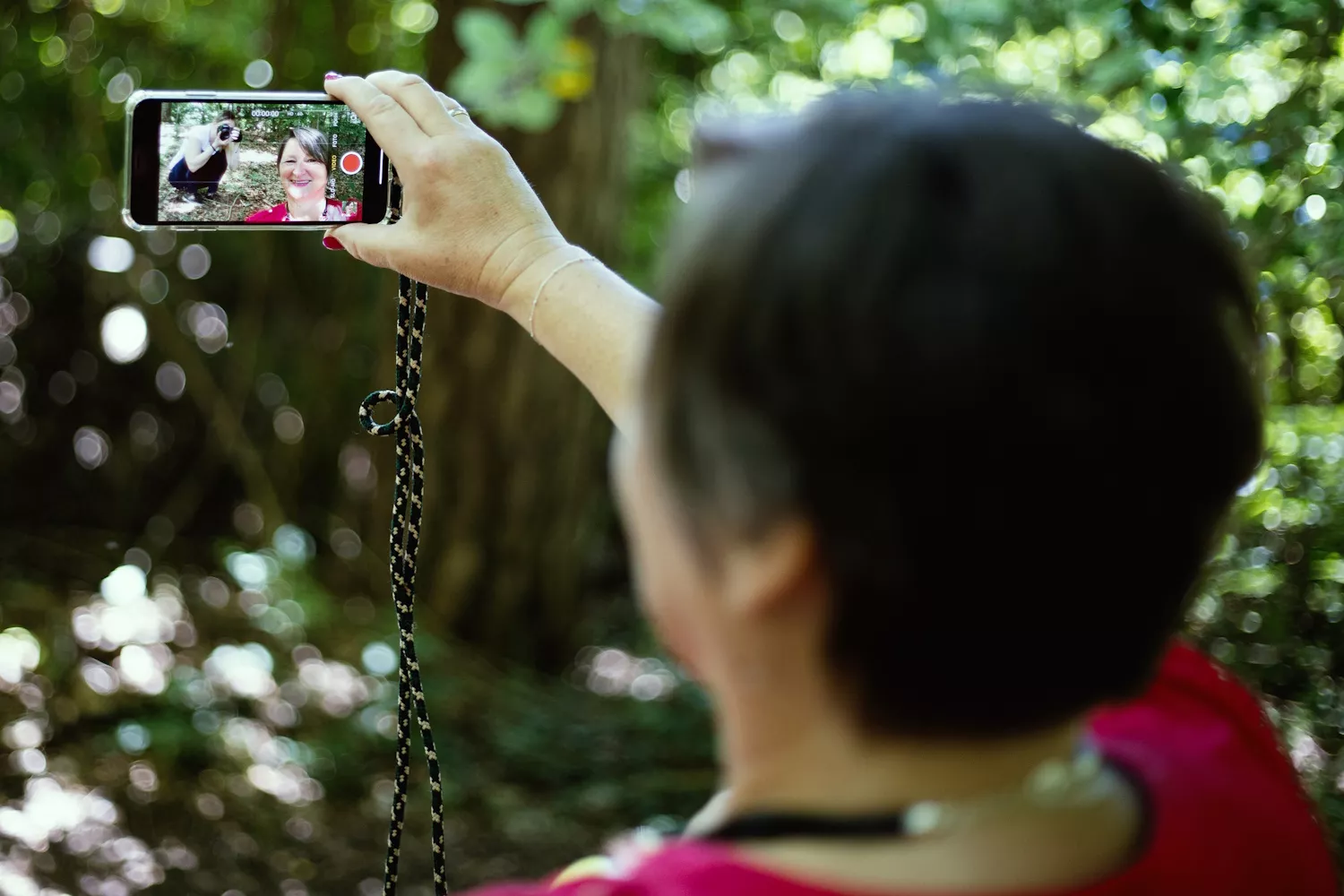 Heike schaut sich selbst bei einer Aufnahme im Smartphone an und dreht dir den Rücken zu