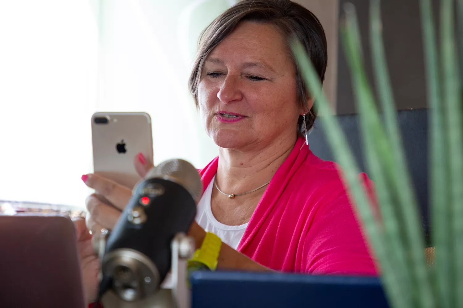 Heike schaut auf Smartphone am Schreibtisch sitzend mit Mikrofon und technischem Equipment vor sich